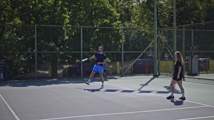 Two friends engage in a friendly and active game of tennis on a sunny outdoor court during the warm summer. They are enjoying their time playing sport and staying fit.