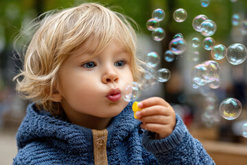 Child blows bubbles outdoors in a park during a sunny day surrounded by greenery