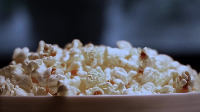 Close up hand taking popcorn from white bowl full of popcorn during movie watching home cinema snack film night cozy evening leisure moment (