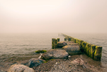 wybrzeże morskie z drewnianym falochronem w porannej mgle