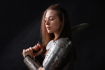 Obraz premium Portrait of a young woman, fantasy warrior in armor with a sword in her hands isolated on a dark background.