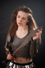 Obraz premium Portrait of a young woman, fantasy warrior in armor with a sword in her hands isolated on a dark background.