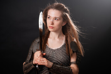 Obraz premium Portrait of a young woman, fantasy warrior in armor with a sword in her hands isolated on a dark background.