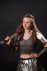 Obraz premium Portrait of a young woman, fantasy warrior in armor with a sword in her hands isolated on a dark background.