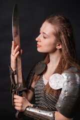 Obraz premium Portrait of a young woman, fantasy warrior in armor with a sword in her hands isolated on a dark background.
