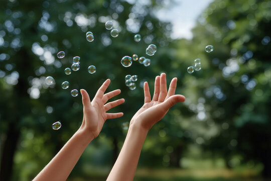 Child hands catching bubbles in park during summer