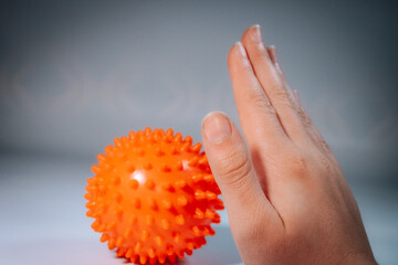 Close-up of a hand holding a bright orange, sharp massage ball used for therapy or exercise, against a soft focus background.
