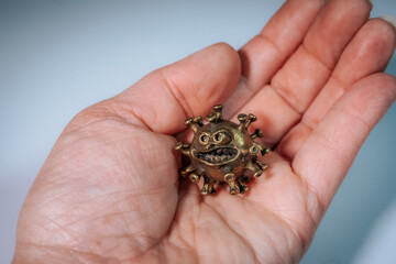 A person gently holds four small bronze-colored virus-like figures with cartoon faces in their palms.