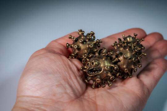 A person gently holds four small bronze-colored virus-like figures with cartoon faces in their palms.