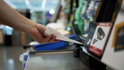 Customer hand taking a paper receipt from a self-service checkout machine in a brightly lit...