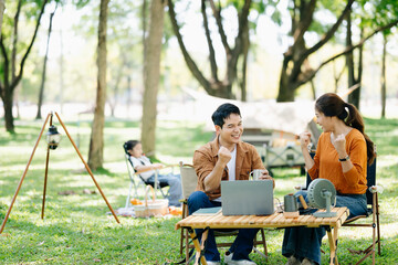 Asian couple enjoys a peaceful camping morning with coffee, breakfast, music, and devices in nature