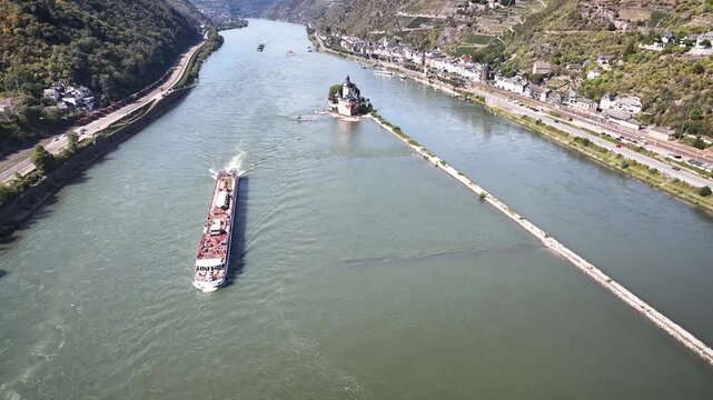 Aerial pull-back shot from Pfalzgrafenstein Castle on its small island in middle of the Rhine River with passing river cruise ship, steep valley slopes, vineyards and riverside town Kaub.
