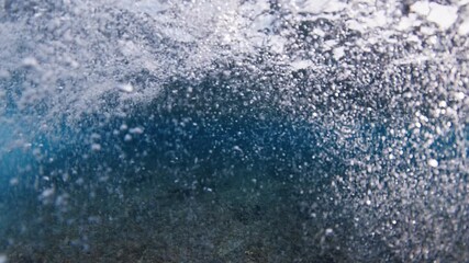 Underwater view of the ocean wave breaking over the shore in the Maldives with ring bubbles forming in front of the camera