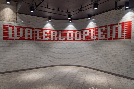 The "Waterlooplein" station name in iconic red typography on a curved, white-tiled wall inside the Amsterdam, Netherlands metro station.