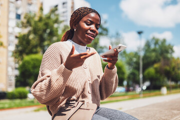 Fototapeta premium Young black woman is using smartphone. She is recording voice message.