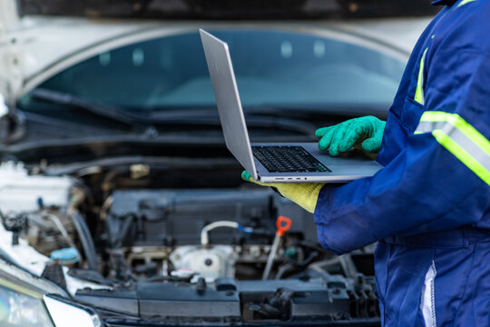African mechanic using a laptop to run diagnostics on a car engine, troubleshoot issues, and monitor vehicle performance in his workshop