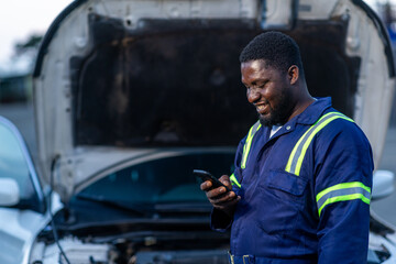 Local African mechanic, small business owner using his smartphone for client video calls, digital banking, and social media in his workshop, SME