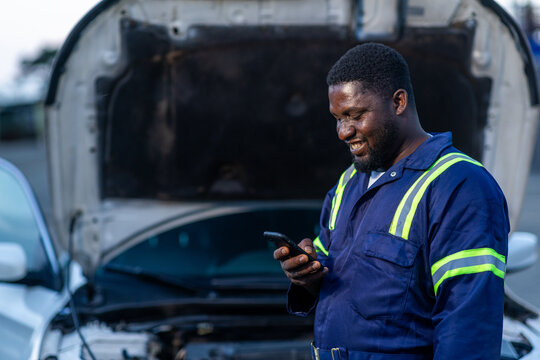 Local African mechanic, small business owner using his smartphone for client video calls, digital banking, and social media in his workshop, SME