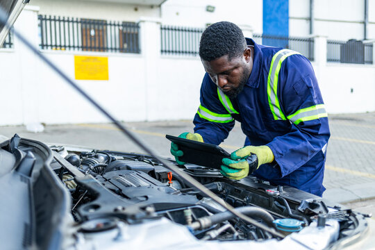 African mechanic using a tablet to inspect a car engine, troubleshoot and perform routine maintenance with digital assistance - Powered by Adobe