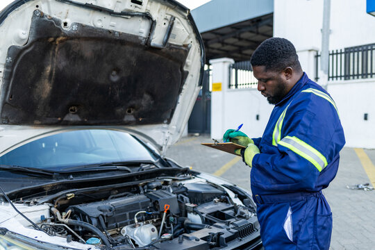 African mechanic recording car diagnostics on a clipboard during routine maintenance in his workshop