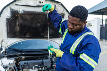 African mechanic checking a car engine oil level with the dipstick