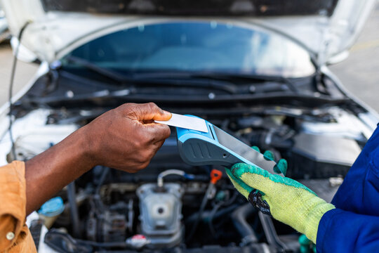 Contactless payment, African mechanic receiving money from a customer via POS terminal for car repair services