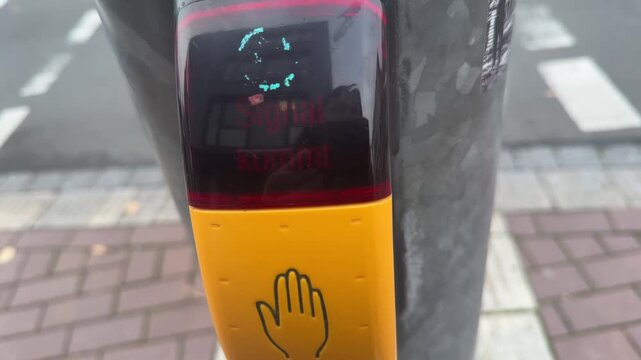 A close-up of an urban traffic light button in Germany with the illuminated German text "Signal kommt" (Signal is coming). The scene focuses on urban mobility and pedestrian crossing technology.