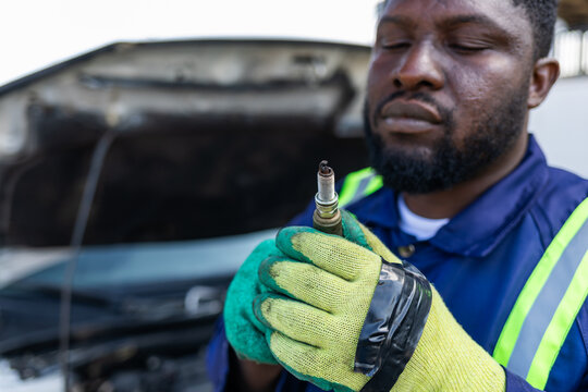 An African mechanic in gloves carefully inspects a dirty spark plug, automotive maintenance and repair