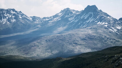 Majestic snow capped peaks tower over rugged terrain, bathed in soft dawn light. Shadows dance across the rocky ground, creating a dramatic mountain scene that inspires awe.