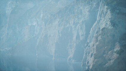 A breathtaking landscape reveals towering cliffs that loom over a tranquil lake. The scene is enveloped in a gentle mist, creating a serene atmosphere perfect for reflection and exploration.