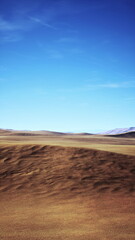 A sweeping view of a vast, barren landscape unfolds under a clear blue sky. Rolling hills of earthy tones stretch across the horizon, evoking feelings of solitude and adventure.