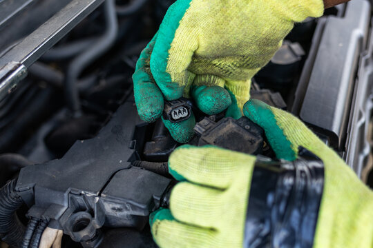 African mechanic holding a disconnected connector in a car engine compartment