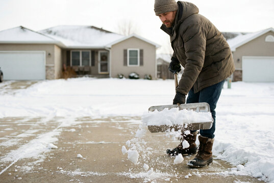 Person shoveling snow in front of a detached house.