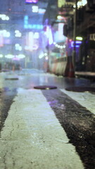 Rain soaked street illuminated by vibrant lights creates a lively atmosphere. The pavement glistens as reflections of neon signs and city life make everything come alive after dusk.