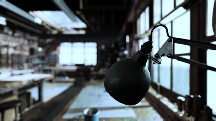A well used workshop showcases natural light streaming through large windows. A vintage desk lamp hangs from the ceiling, illuminating a space filled with tools and materials for various crafts.