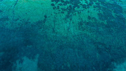 Aerial perpendicular view of the sea surface. The ocean's colors range from turquoise to blue....