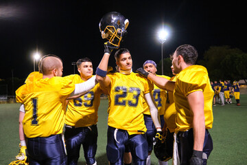 American football players in uniform cheering, holding helmet up, celebrating triumph after game