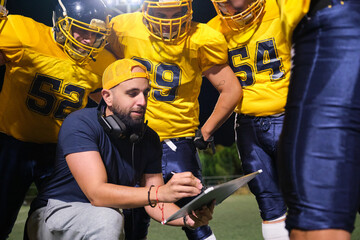 Coach explaining play to American football players during night practice on field © Ladanifer