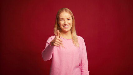 Fototapeta premium Smiling cheerful blonde woman nodding yes with head showing thumb up isolated on red background