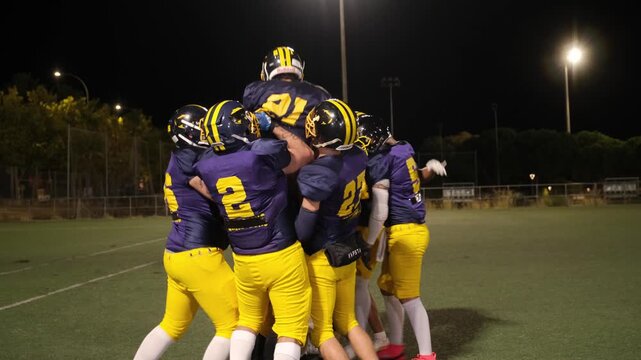 Victorious football team celebrating together on the field after scoring during a night game