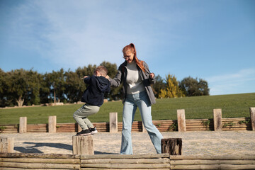 Mother supporting son balancing on wooden logs outdoors