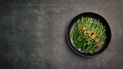 Stir-fry green beans with sesame and garlic on black background, top view, copy space