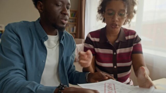 Young adult Biracial couple sorting bills and receipts in folder while managing finances together, organizing budget and household expenses carefully at home