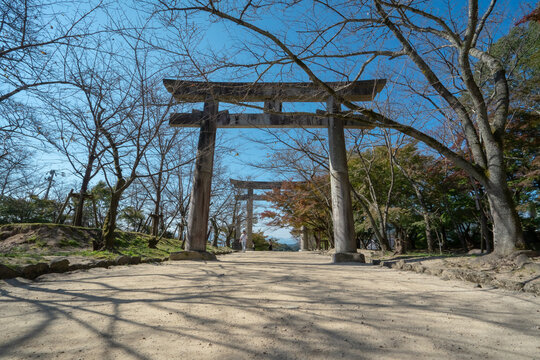 Wooden Torii gates line a dirt path leading toward a distant mountain view under clear sky - Powered by Adobe