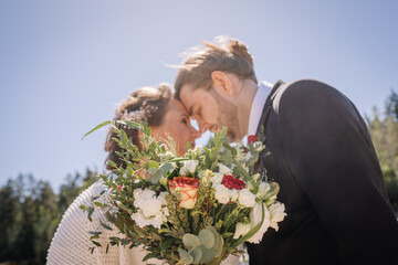 Couple embracing with foreheads touching, surrounded by nature, holding a beautiful bouquet of roses and greenery, capturing the essence of love and commitment in a romantic moment