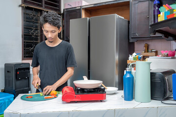 Indonesian southeast asian man cutting vegetables on a cutting board in the kitchen. Prepare to cook