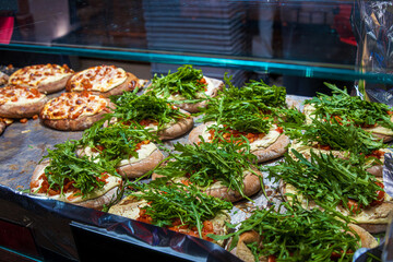 Freshly prepared flatbread with melted cheese and generous arugula topping displayed at a festive winter market food stall