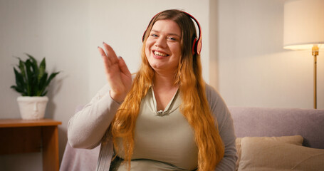 Plus size woman waves at camera talking on smartphone smiling