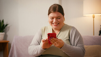 Plus size woman laughs watching funny videos on smartphone
