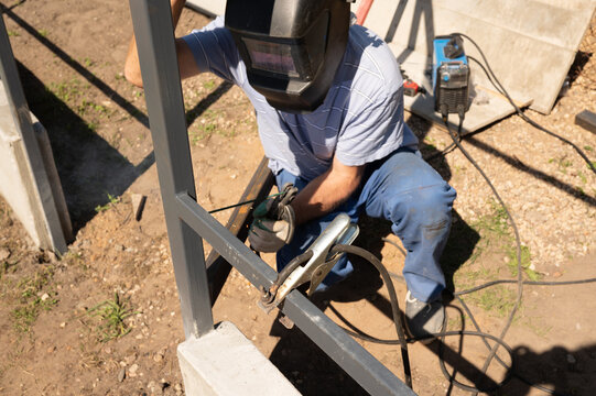 Adult caucasian male welding metal frame outdoors in protective gear. National Welding Month - Powered by Adobe